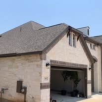 Exterior of a house with a brown roof and tan brick facade; garage door open.