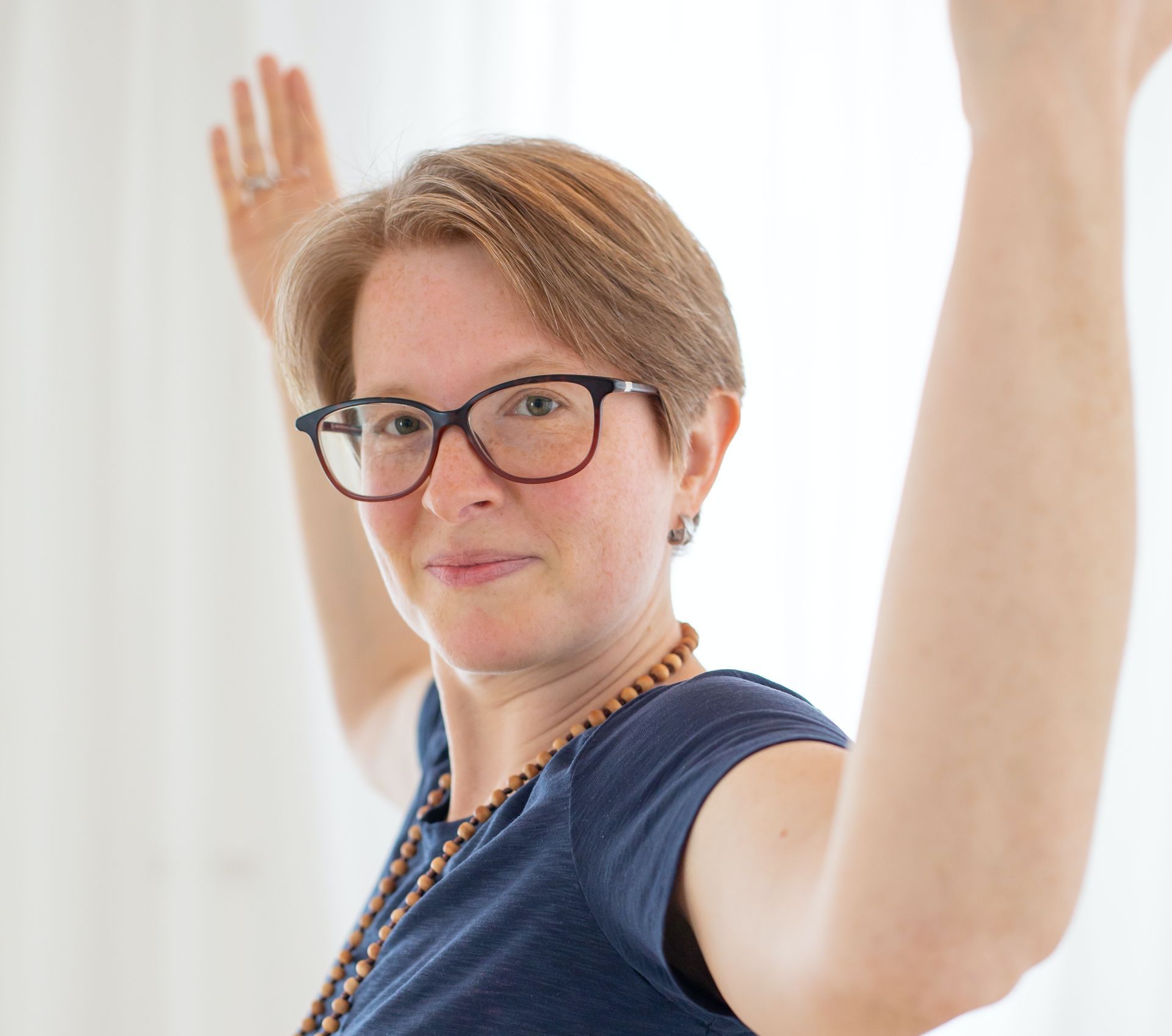 Eine Frau mit Brille und Halskette streckt ihre Arme in die Luft