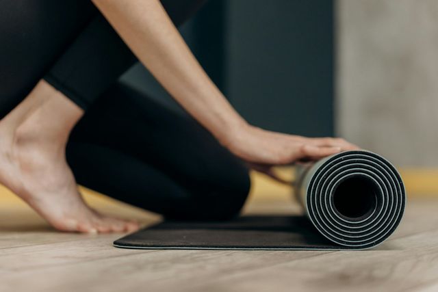 Eine Frau rollt eine Yogamatte über den Boden.