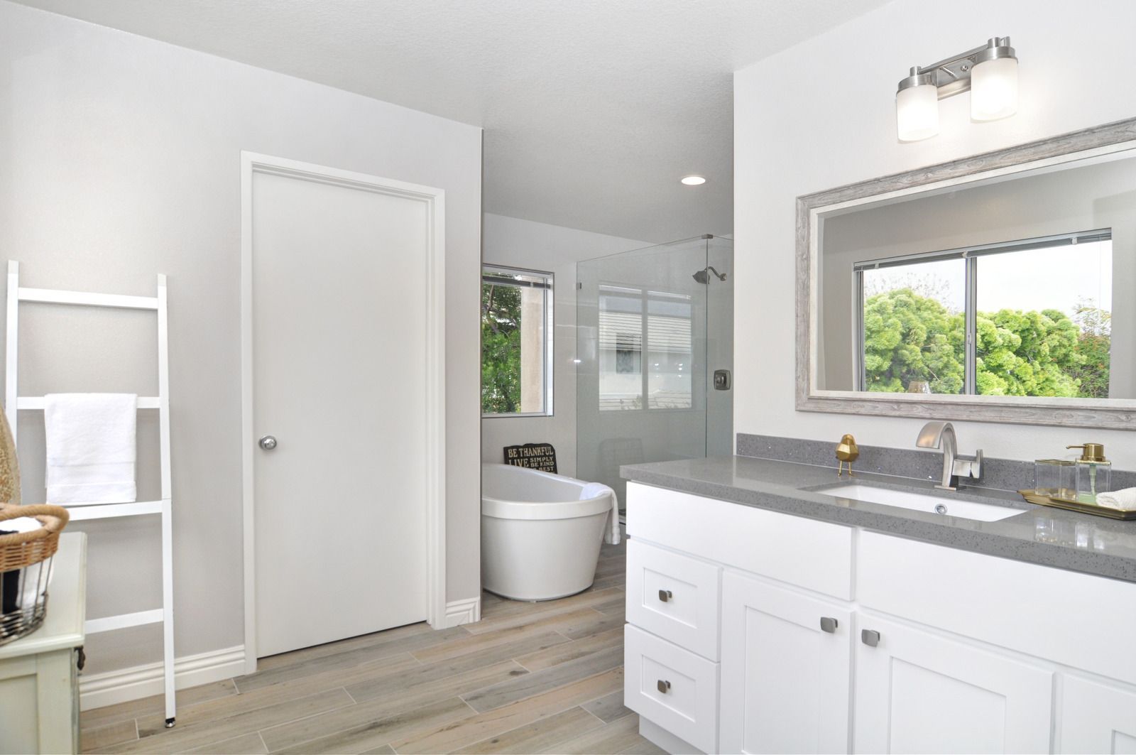 Bright bathroom with white vanity, gray countertop, large mirror, and soaking tub.