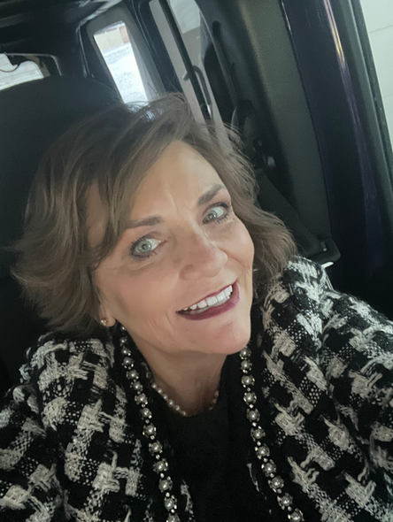 A woman in a black and white jacket is smiling for the camera while sitting in a car.