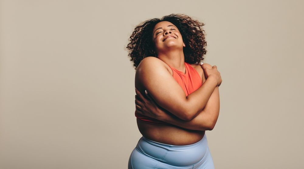 A woman is hugging herself with her arms crossed and smiling.