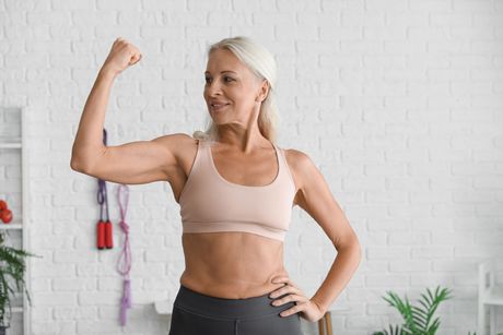 An older woman is flexing her muscles in a living room.