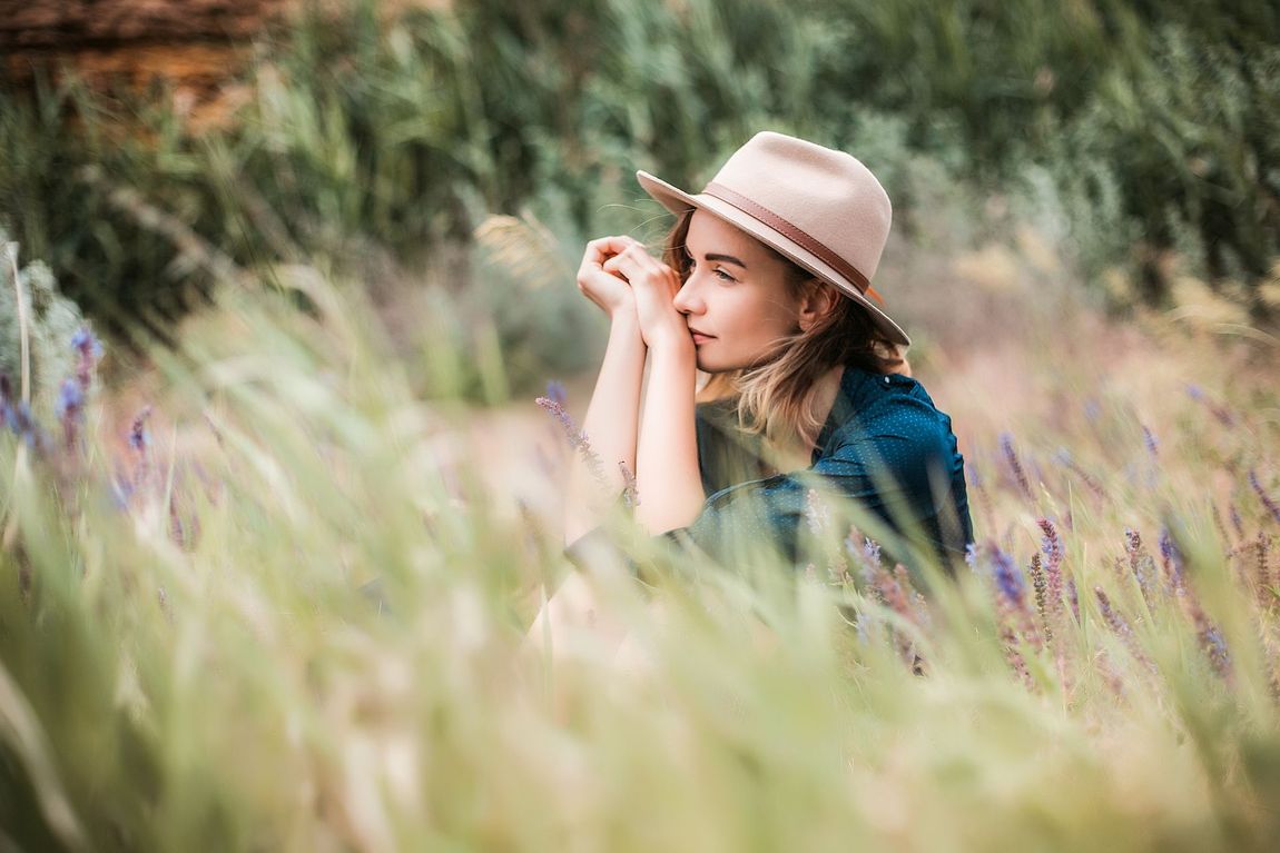 A woman in a hat is sitting in a field of tall grass.