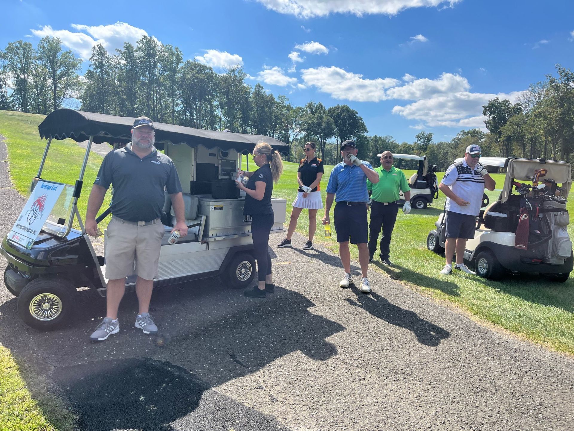 A group of people are standing next to a golf cart on a golf course.