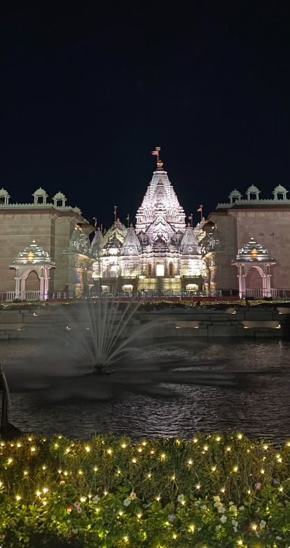 A temple is lit up at night with a fountain in front of it.
