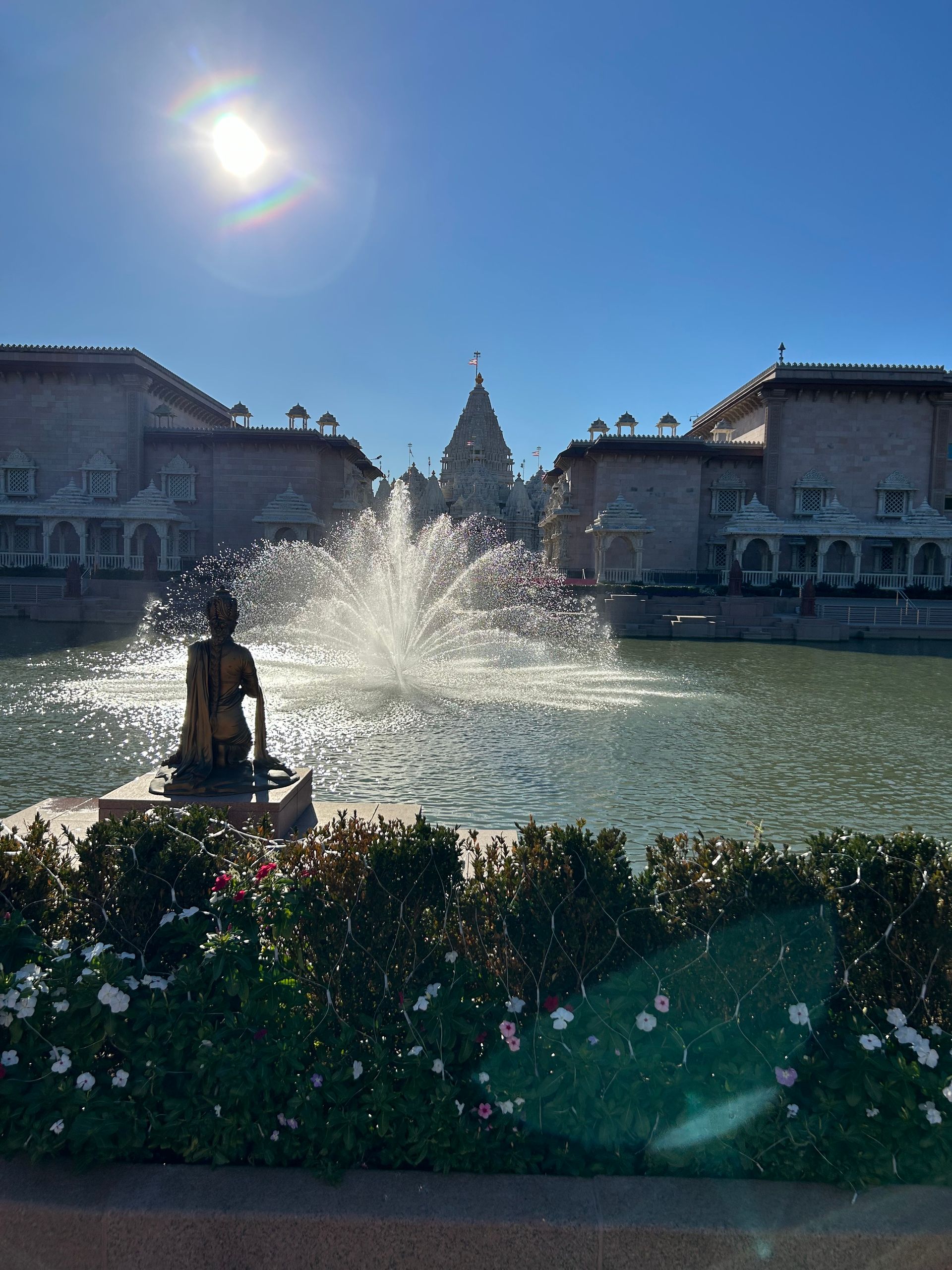 A fountain with a statue in the foreground and buildings in the background.