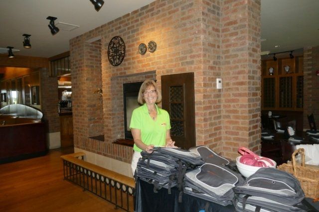 A woman in a green shirt is standing in front of a pile of backpacks.