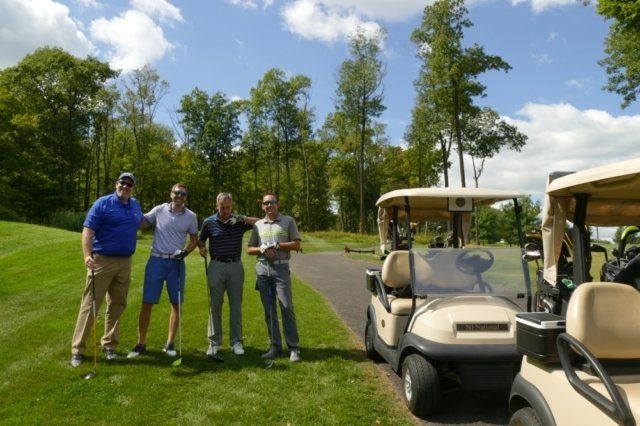A group of men standing next to a golf cart on a golf course.