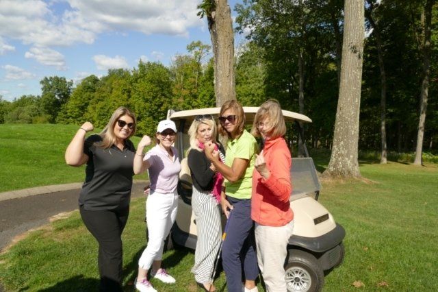 A group of women are standing next to a golf cart on a golf course.