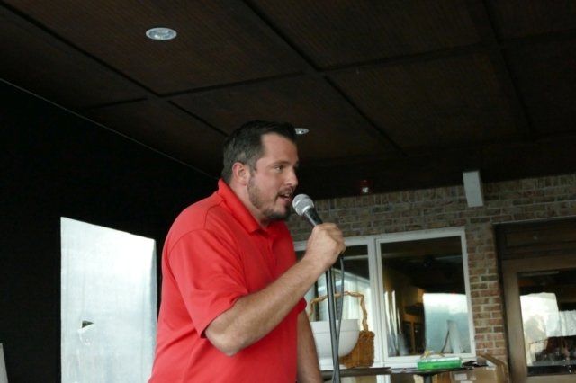 A man in a red shirt is speaking into a microphone