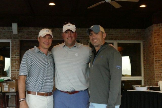 Three men posing for a picture in front of a brick wall