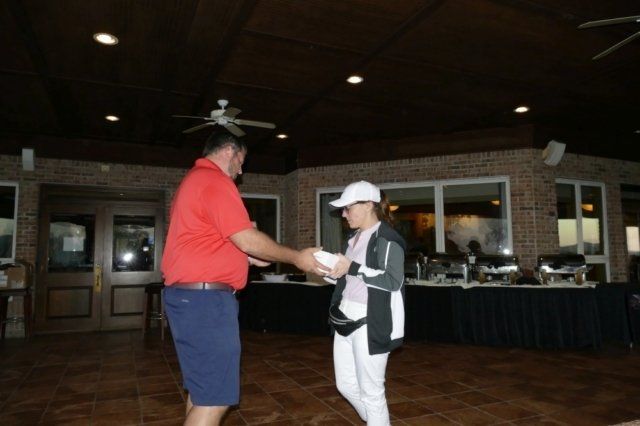 A man in a red shirt is shaking hands with a woman in a white hat