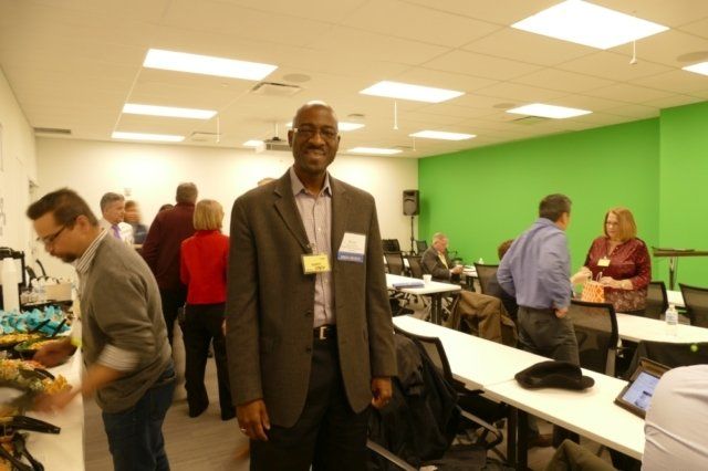 A man in a suit stands in front of a green wall