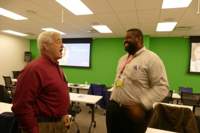 Two men are talking in a room with a green wall