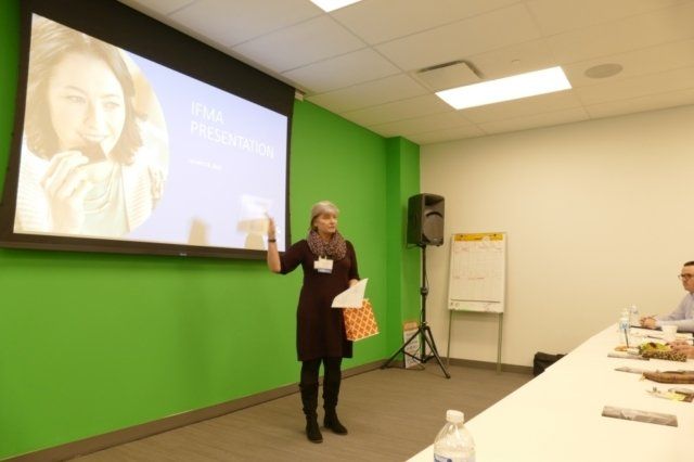 A woman is giving a presentation in front of a green wall