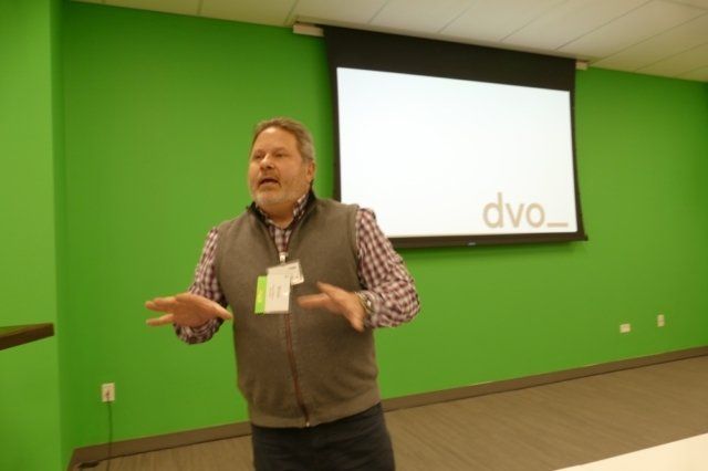 A man is standing in front of a projector screen that says dvo