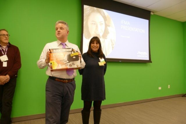 A man and a woman standing in front of a green wall holding a box