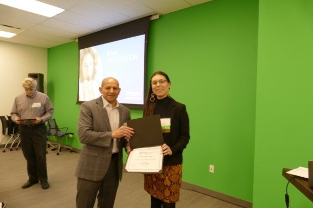 A man and a woman are standing in front of a green wall holding a certificate