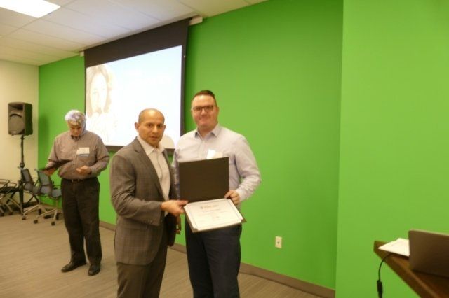 Two men standing in front of a green wall holding a certificate