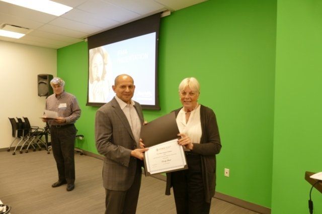 A man is giving a certificate to a woman in front of a green wall