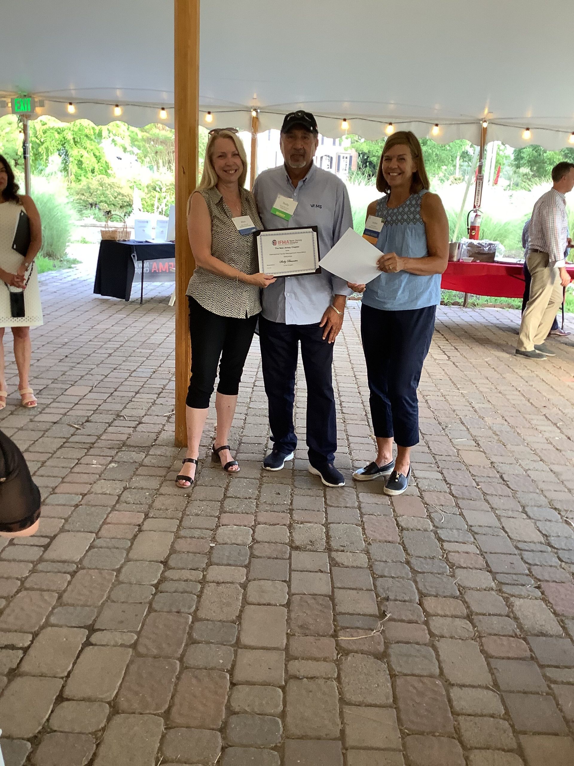 A man and two women are standing under a tent holding a certificate.