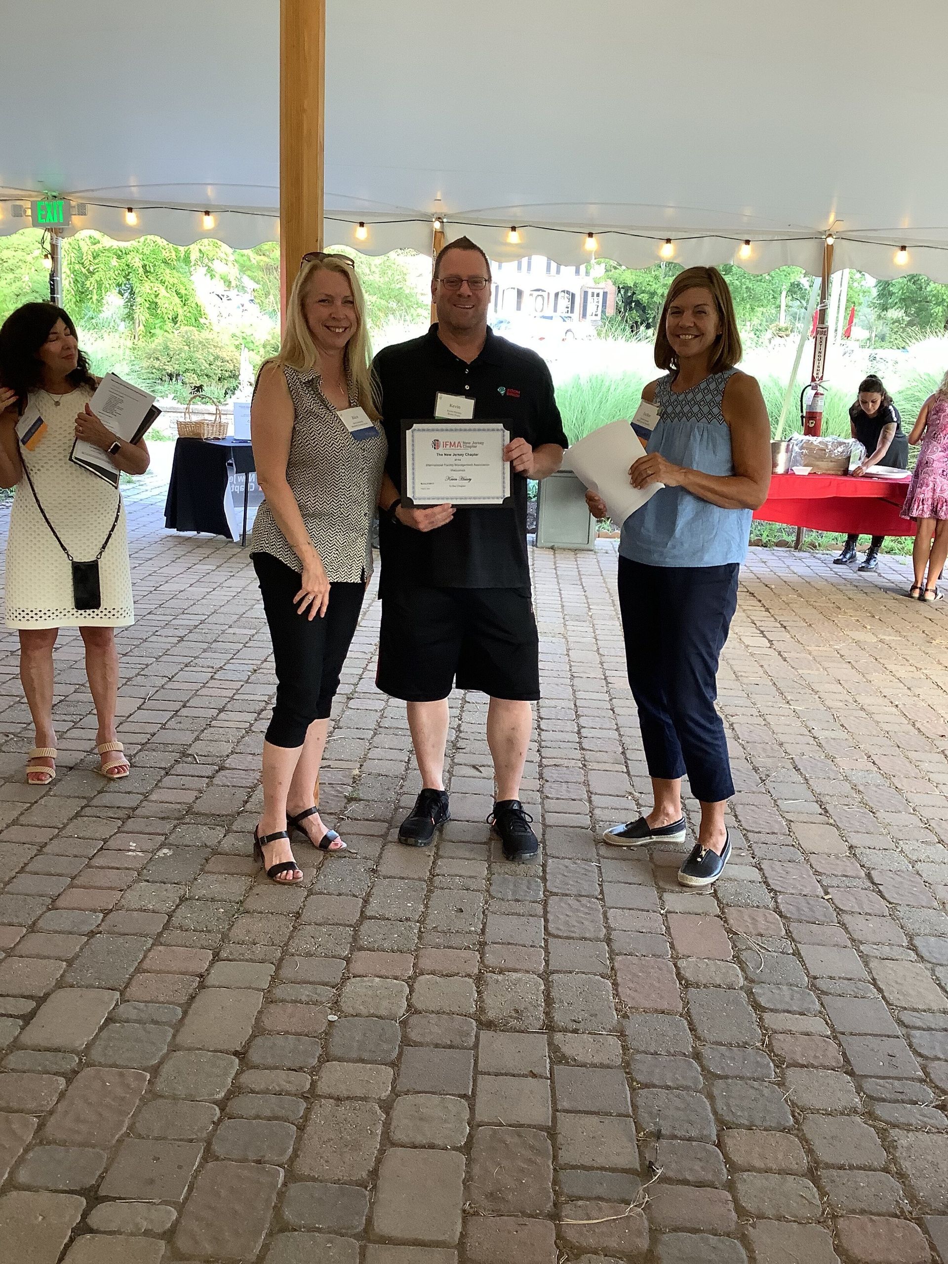 A group of people standing on a brick floor under a tent.