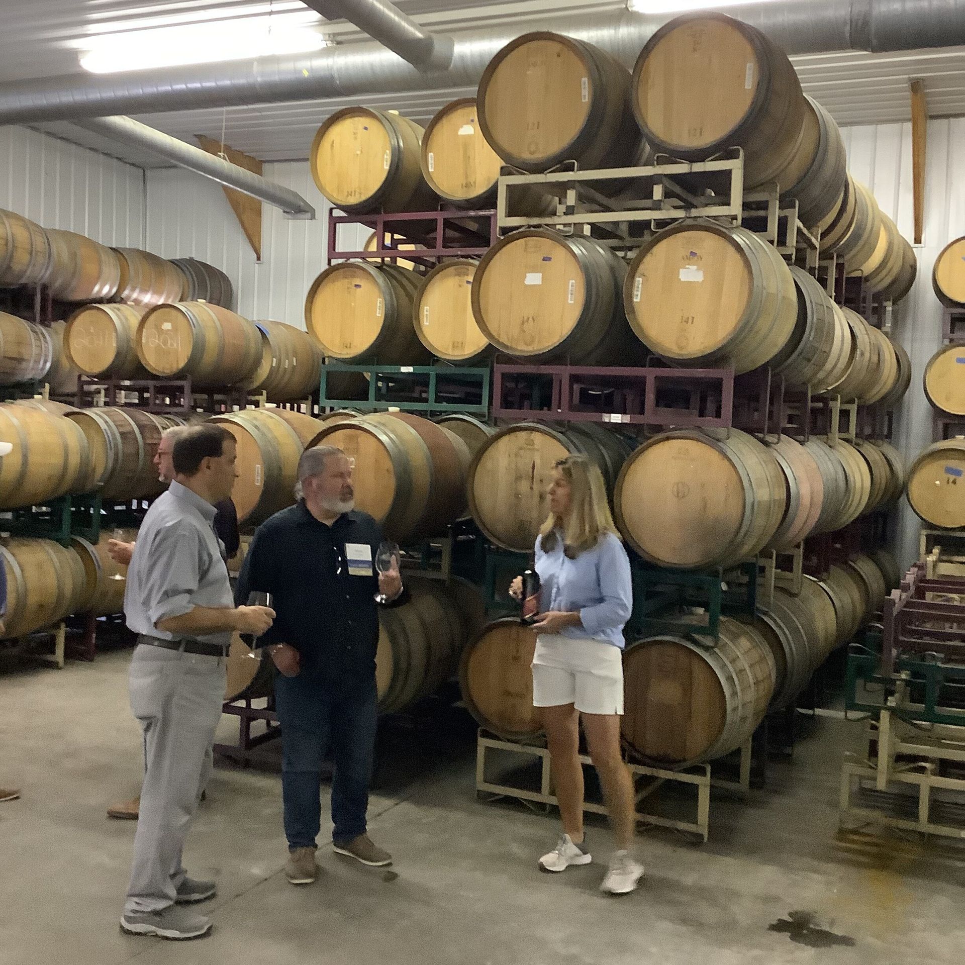 A group of people are standing in a room filled with lots of barrels
