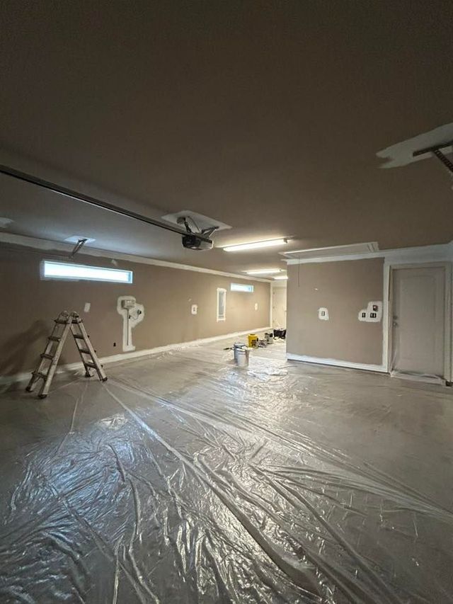 Garage interior under renovation with plastic-covered floor, ladder, and tools under fluorescent lights