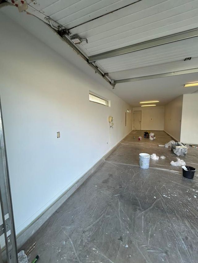 Empty garage interior with white walls, concrete floor, and cleaning supplies near the back wall