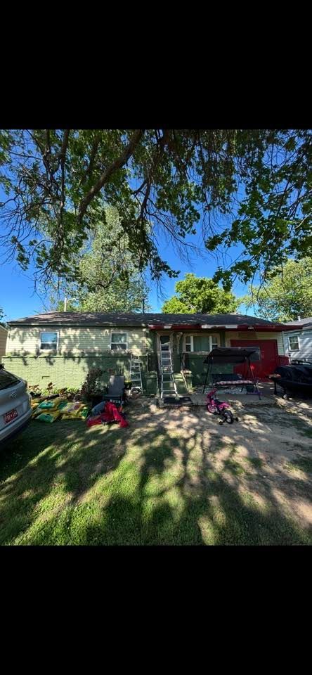 Front yard of a house with large tree shade, patio chairs, and a red car on a sunny day