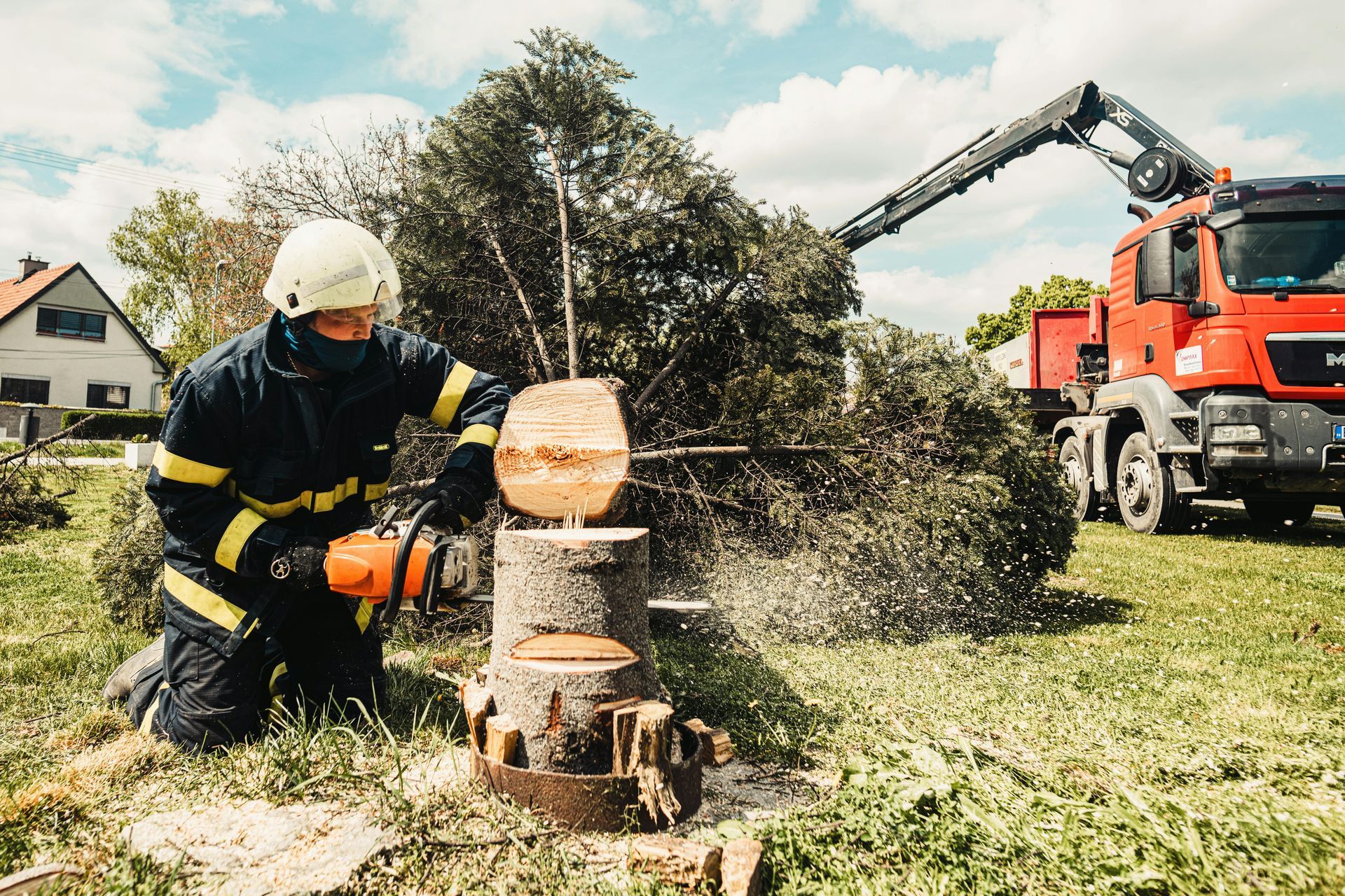 Firefighter using a chainsaw to cut a tree trunk; a truck with an extendable arm is behind him.