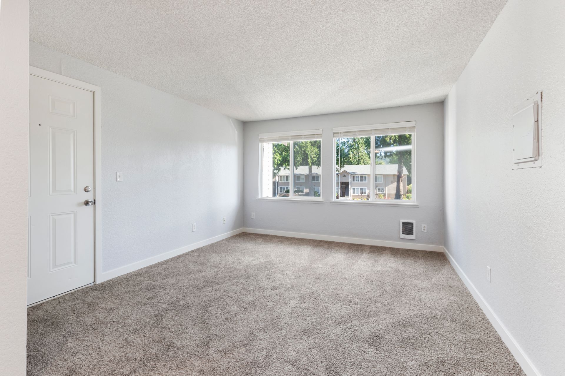 An empty living room with a carpeted floor and three windows.