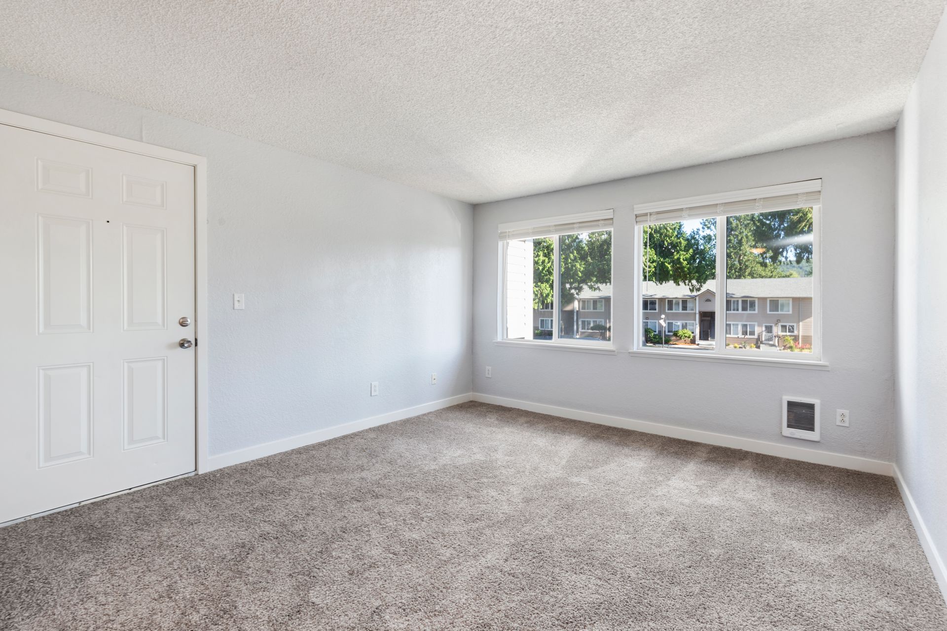An empty living room with a carpeted floor and two windows.