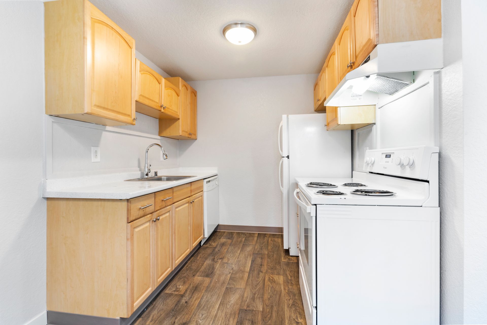 A kitchen with wooden cabinets , a white stove , a refrigerator , and a sink.