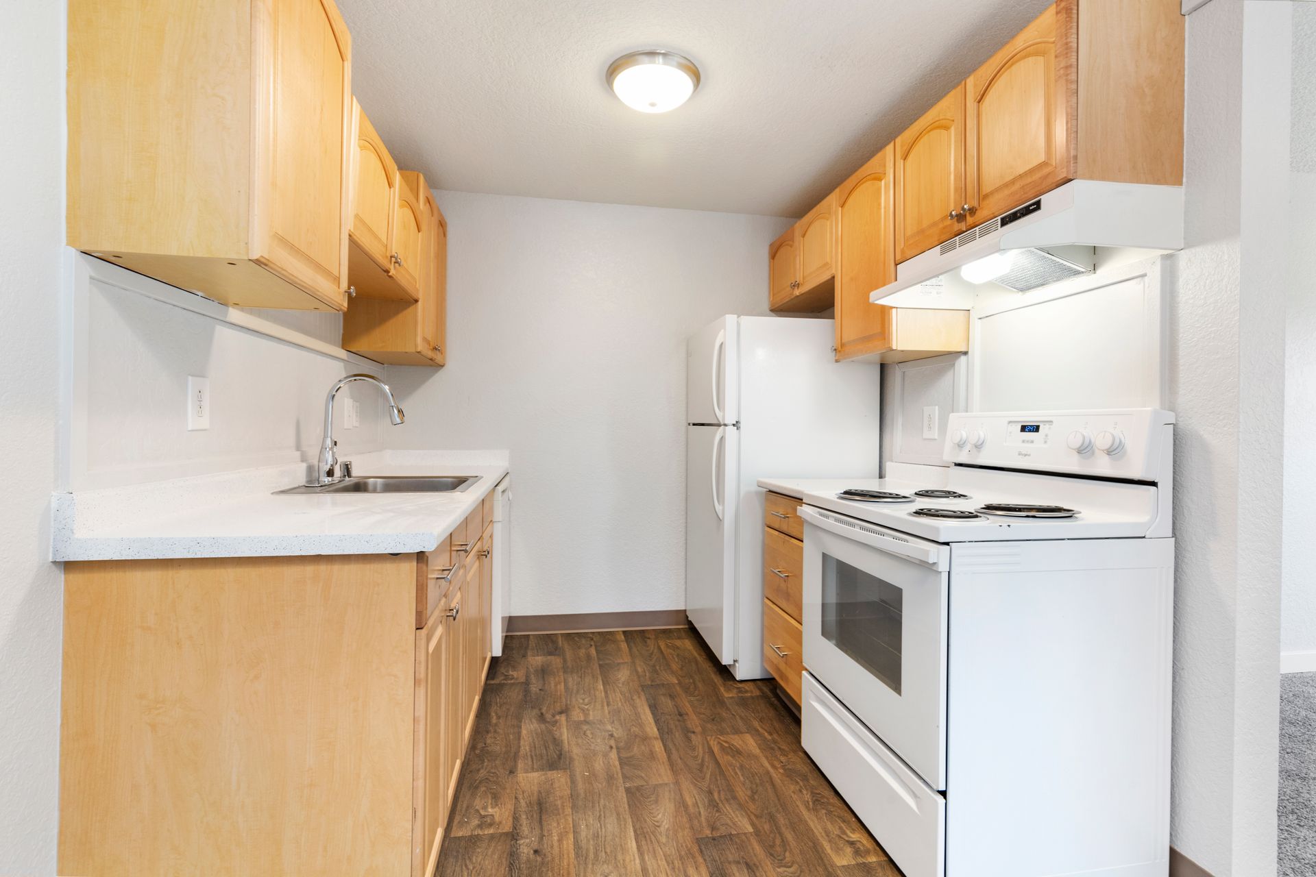 A kitchen with wooden cabinets , a white stove , a refrigerator , and a sink.