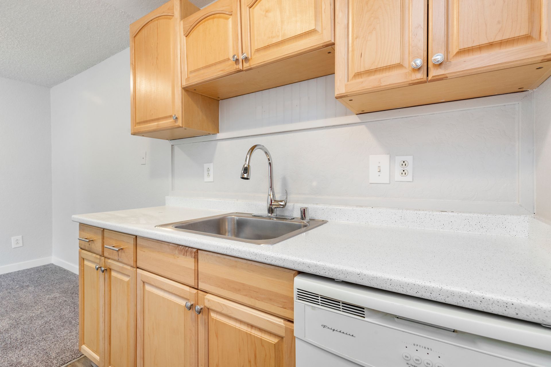 A kitchen with wooden cabinets , a sink , and a dishwasher.