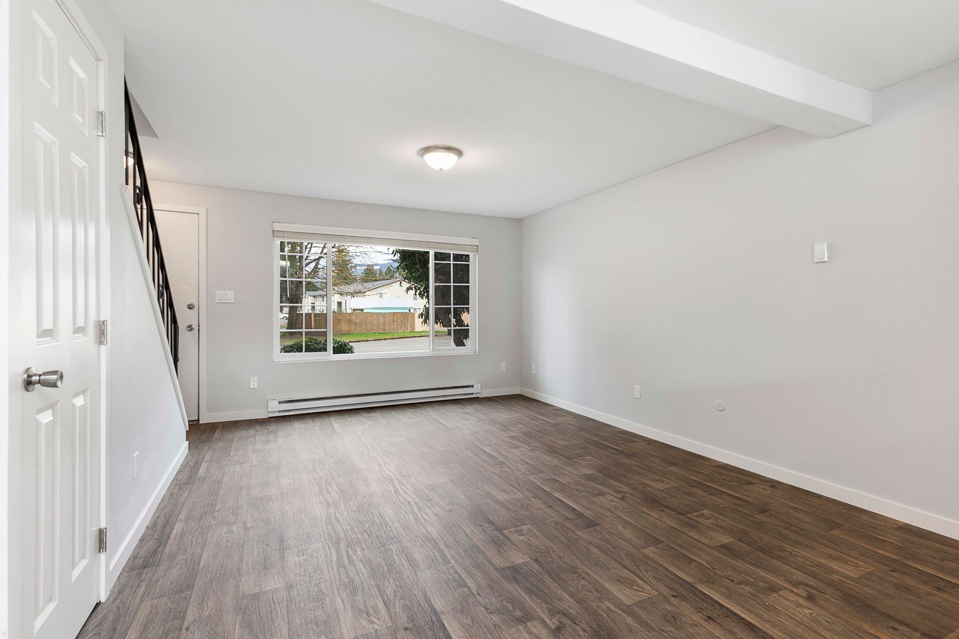 An empty living room with hardwood floors and a large window.
