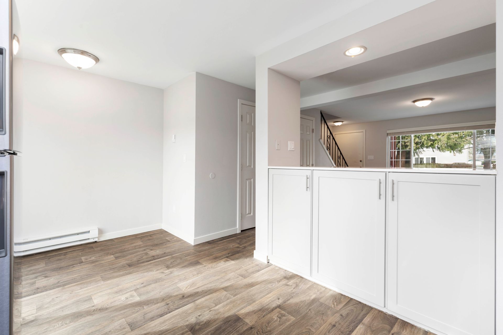 An empty living room with hardwood floors and white cabinets.