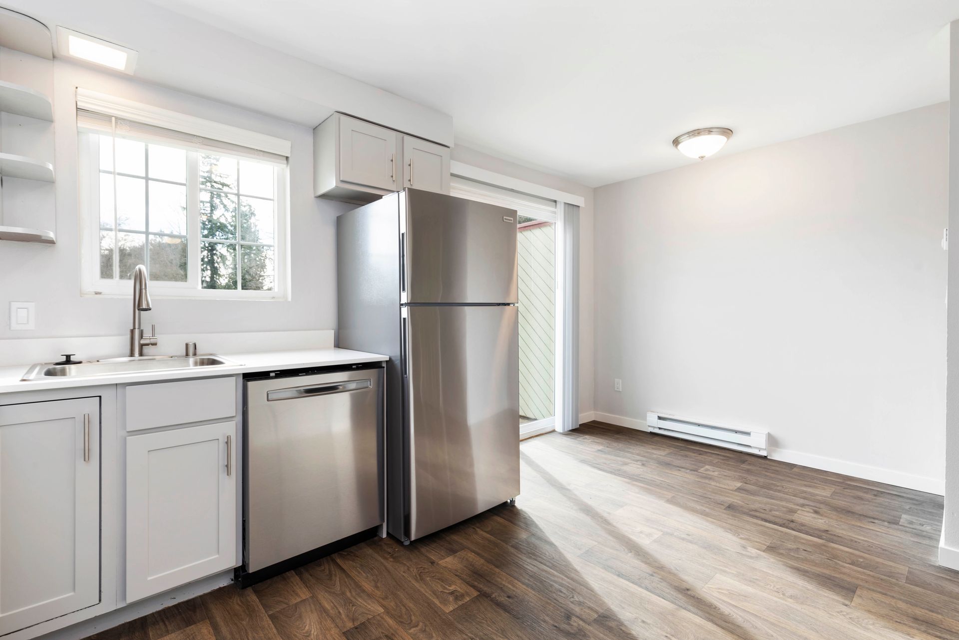 An empty kitchen with a stainless steel refrigerator , dishwasher , sink and window.