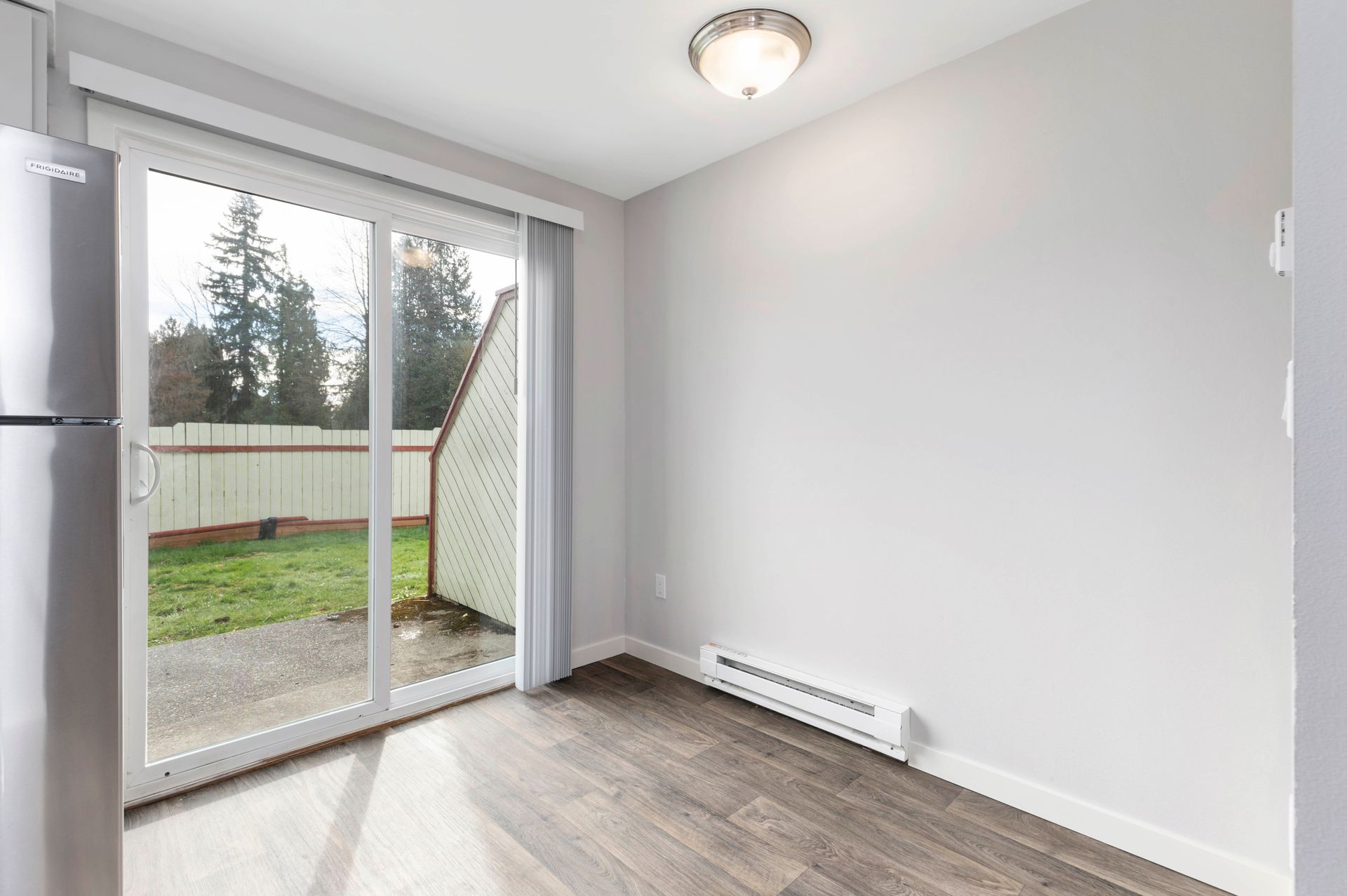 An empty room with a sliding glass door and a refrigerator.