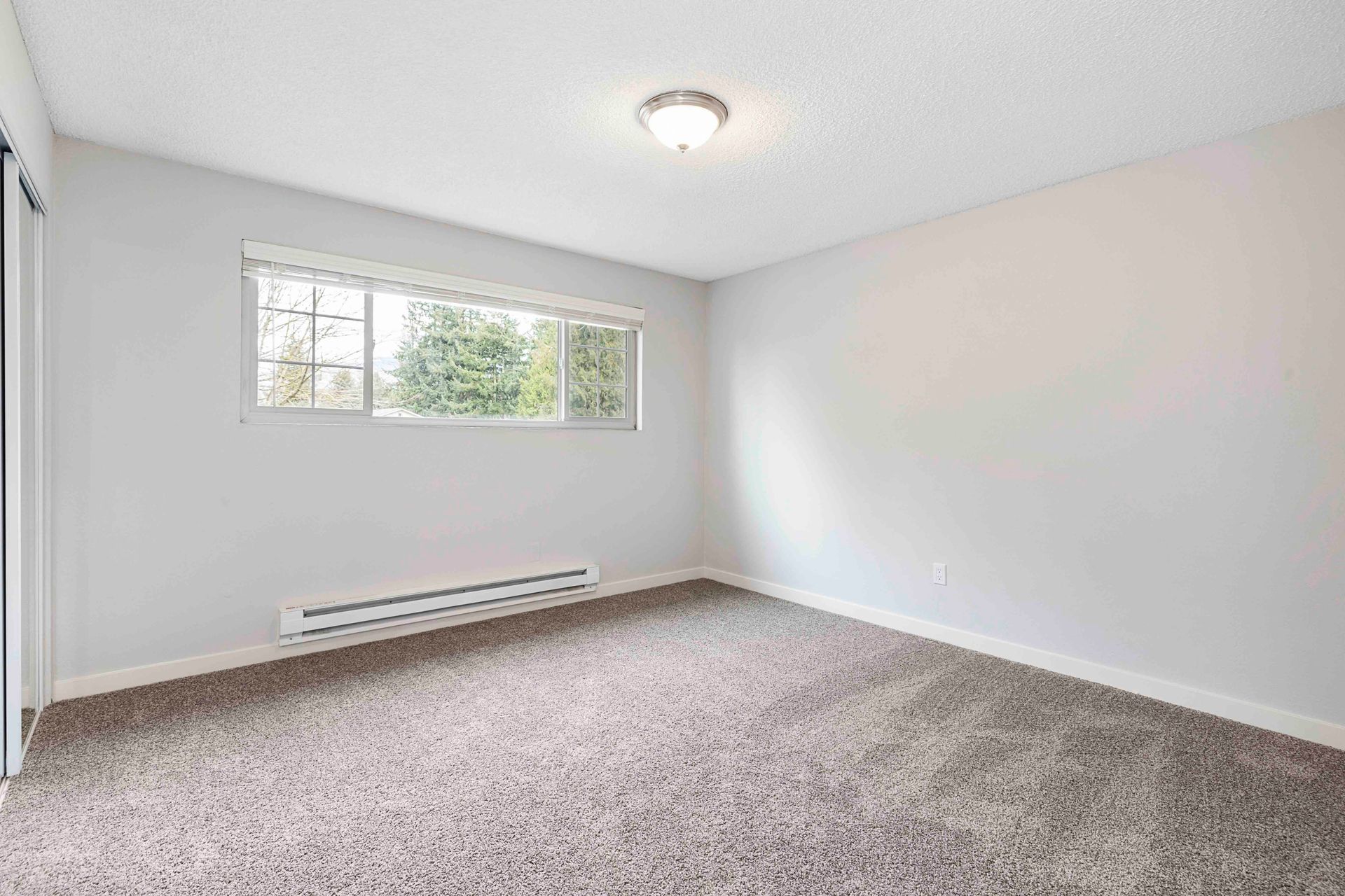An empty bedroom with a window and a carpeted floor.