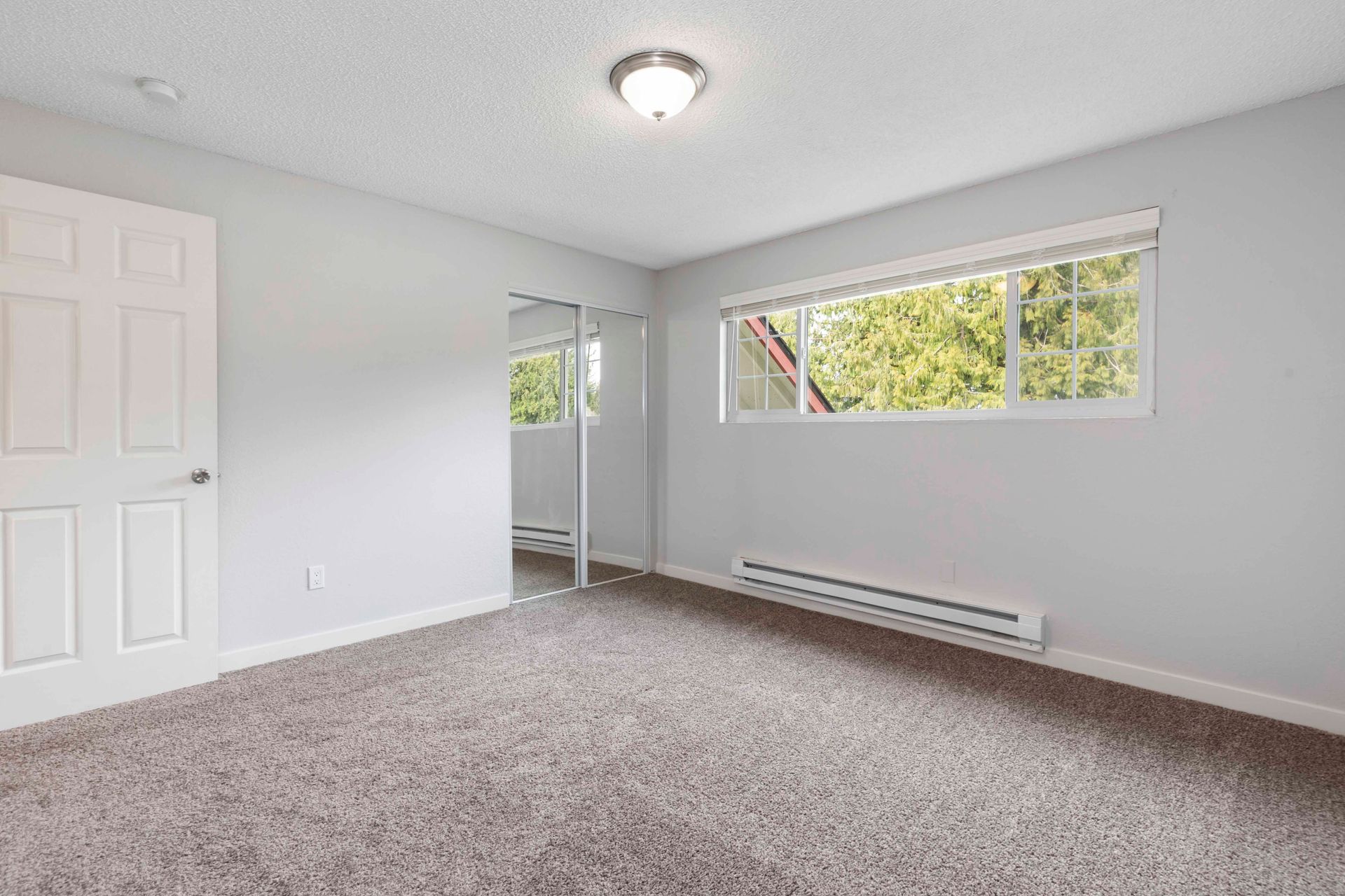An empty bedroom with a window and a carpeted floor.
