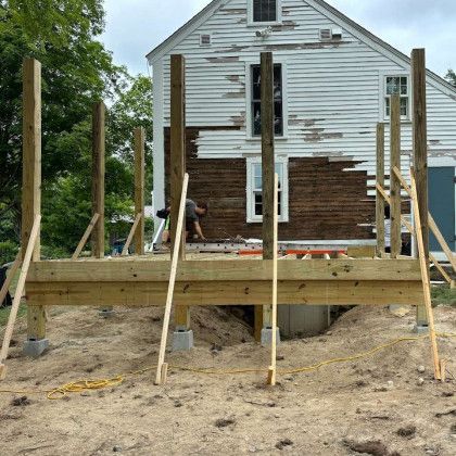 Deck under construction next to a weathered white house; a person works on the structure.