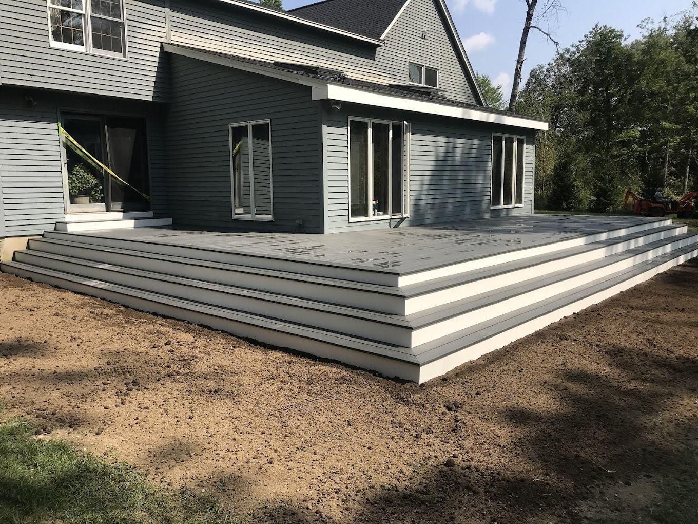 Gray and white deck with steps attached to a teal house; brown soil in the foreground.