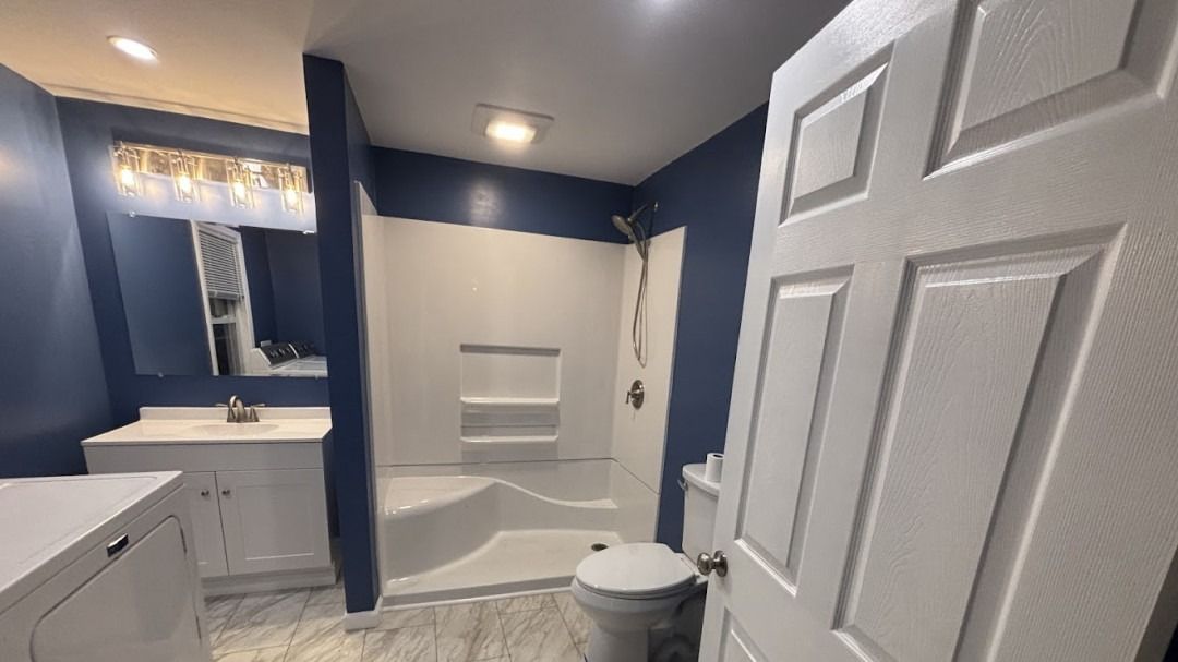 Blue and white bathroom with shower, toilet, vanity, and partially open white door.