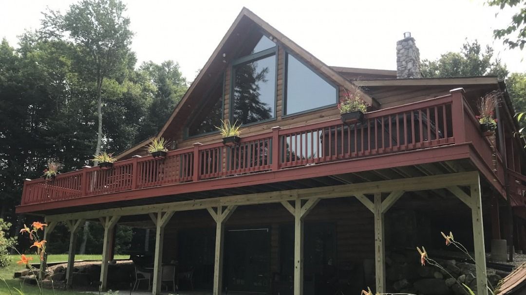 Wooden cabin with red deck, large triangular window, and outdoor covered space.
