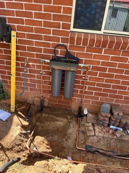 A Water Filter is Being Installed on the Side of a Brick Building — Peel Valley Plumbing In Hillvue, NSW