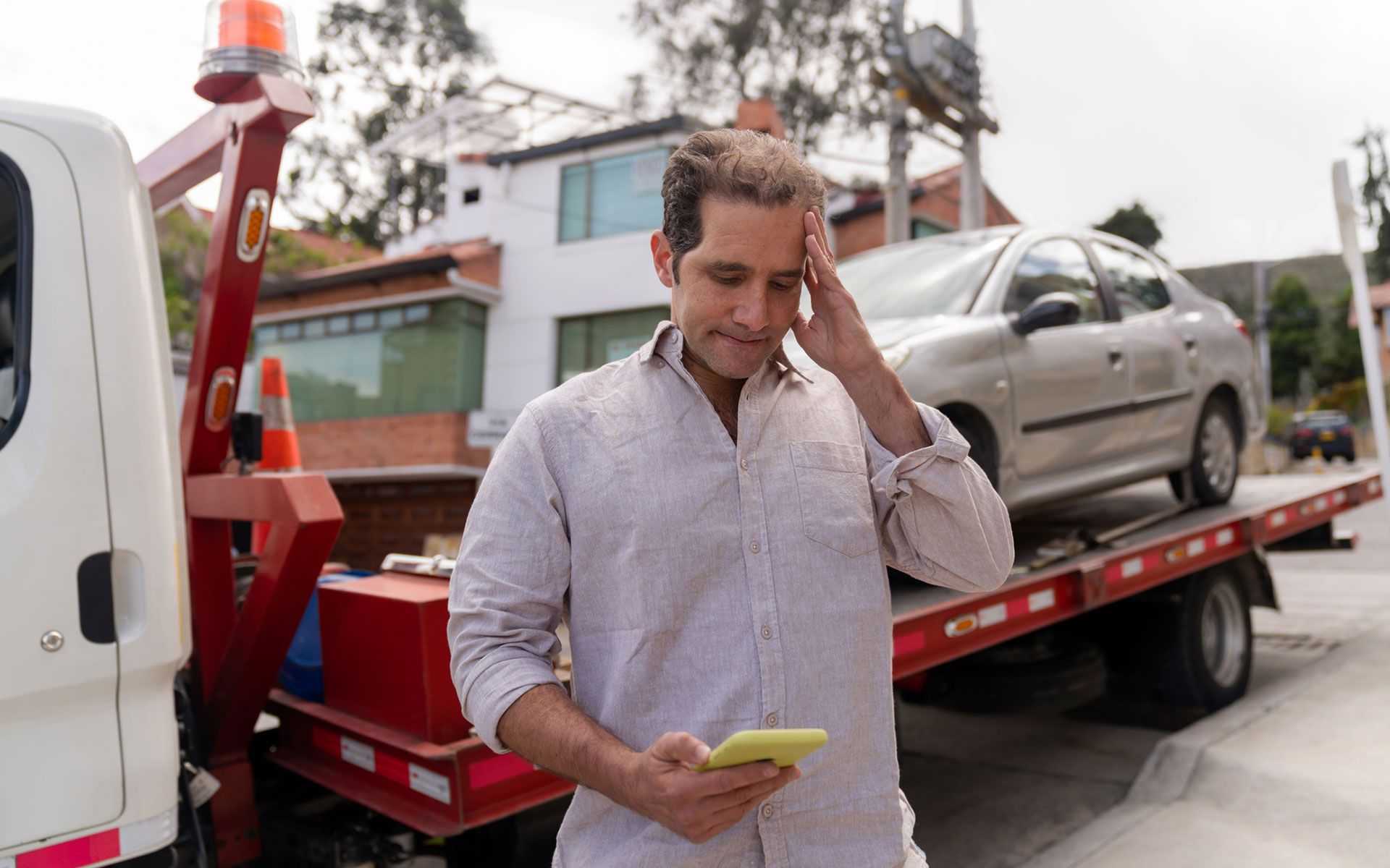 A man is standing in front of a tow truck looking at his cell phone.