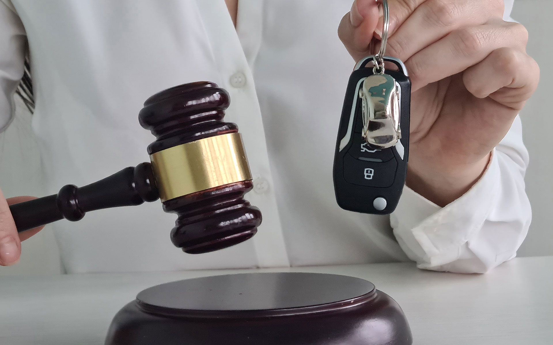 A person is holding a car key in front of a judge 's gavel.